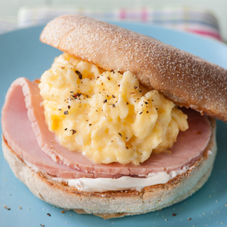 English muffin toast spread with soft cheese, topped with ham and scrambled eggs.